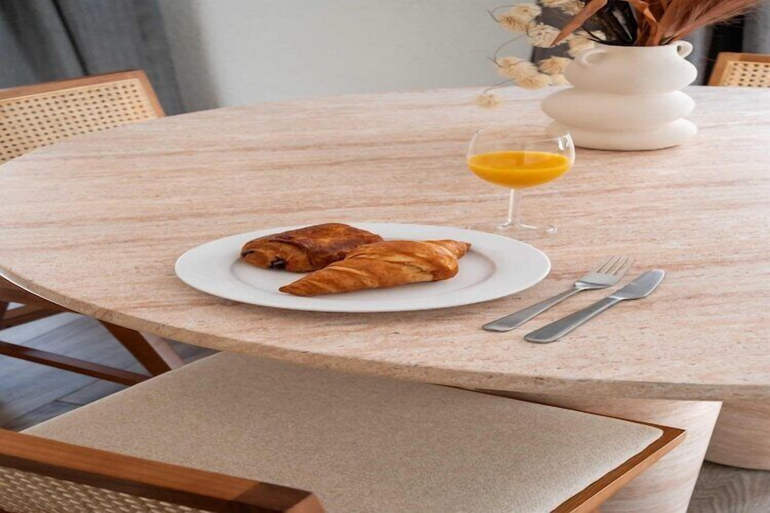 Une table ronde avec une assiette de croissants et un verre de jus d’orange.