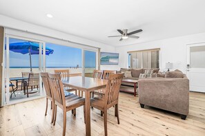 A room with a wooden dining table, chairs, a sofa, and a ceiling fan.