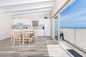 Enjoy a meal on the balcony with a view of the beach, surrounded by a dining area with a round table and comfortable seating.