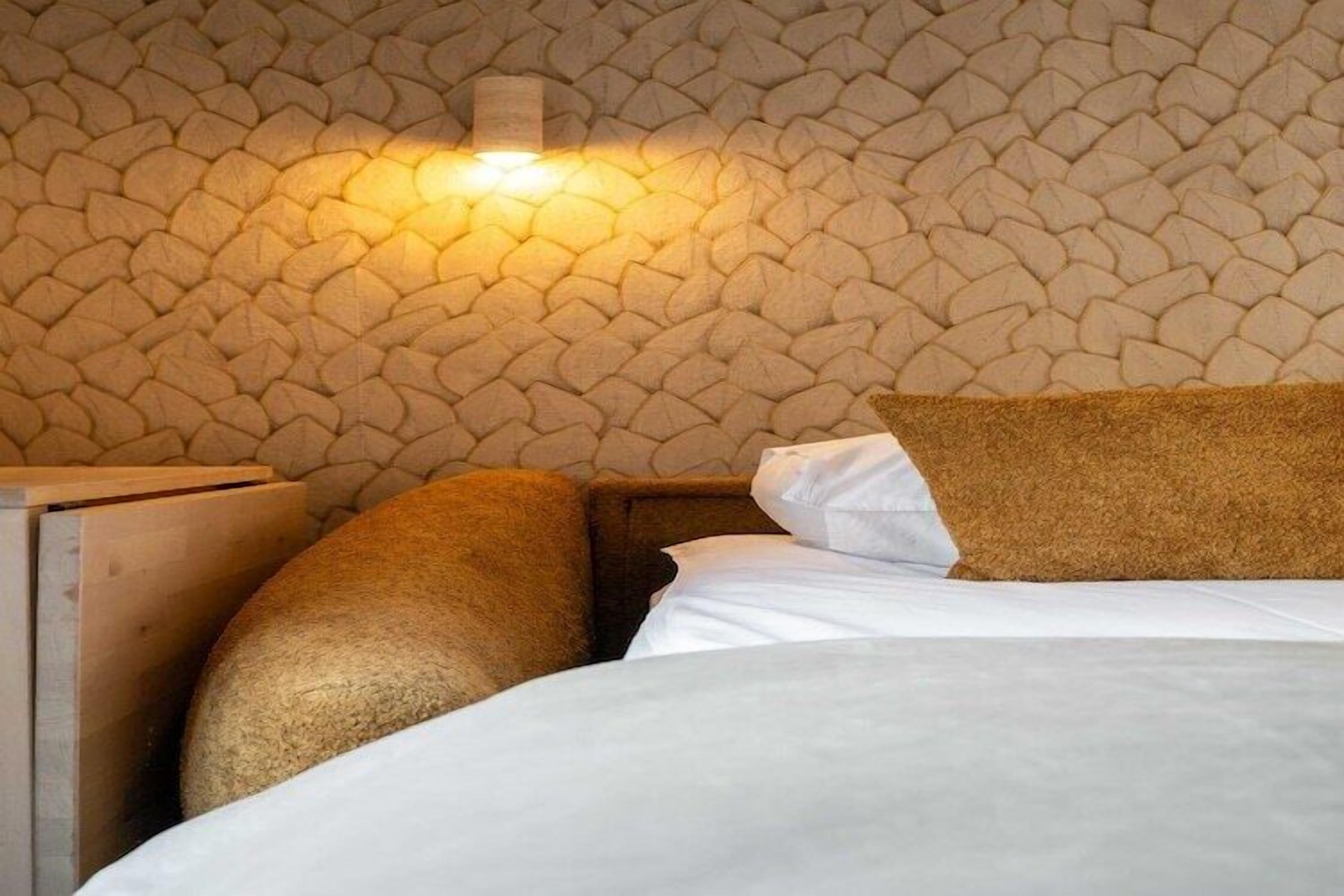 A bed with white linens and a textured wall behind it.
