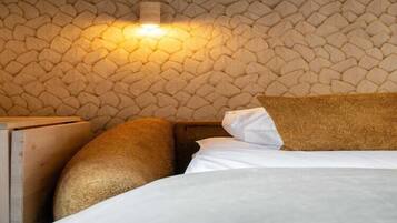 A bed with white linens and a textured wall behind it.