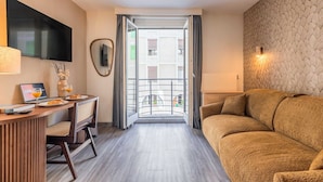 A hotel room with a sofa, a desk with a laptop and glasses, a TV, and a balcony with curtains. - Appartement moderne - AC-1BR-4P- Genève (Genève)