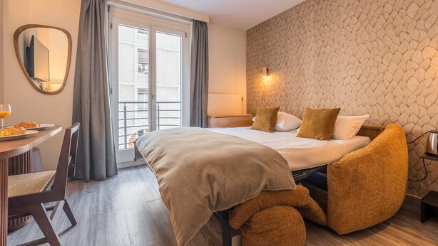 A hotel room with a bed, a desk with a chair, a mirror, and a window with curtains. - Appartement moderne - AC-1BR-4P- Genève (Genève)