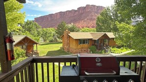 A barbecue grill on a wooden deck with a view of a rustic cabin and a mountain in the background.