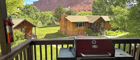 A barbecue grill on a wooden deck with a view of a rustic cabin and a mountain in the background.