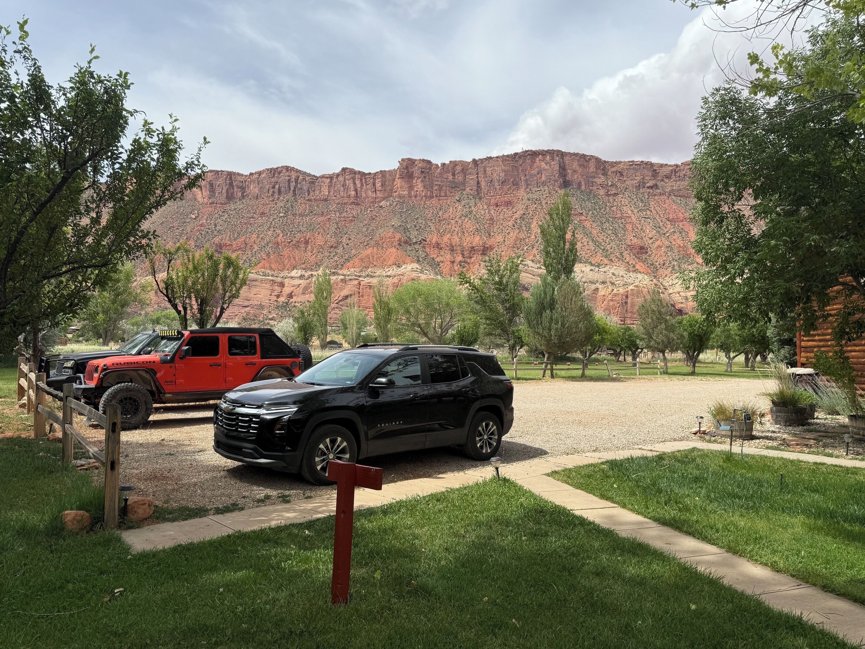 A parking area with two SUVs, a red and a black, in front of a mountain backdrop.