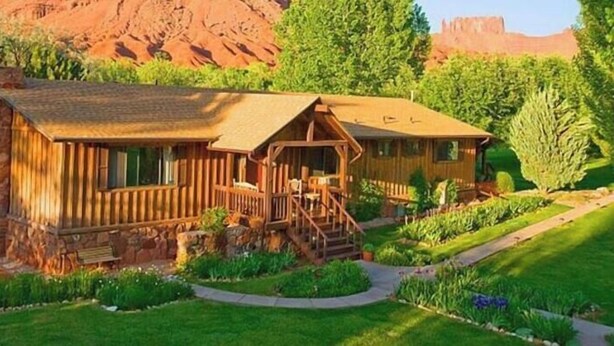 A rustic cabin with a stone chimney, wooden deck, and a small porch.