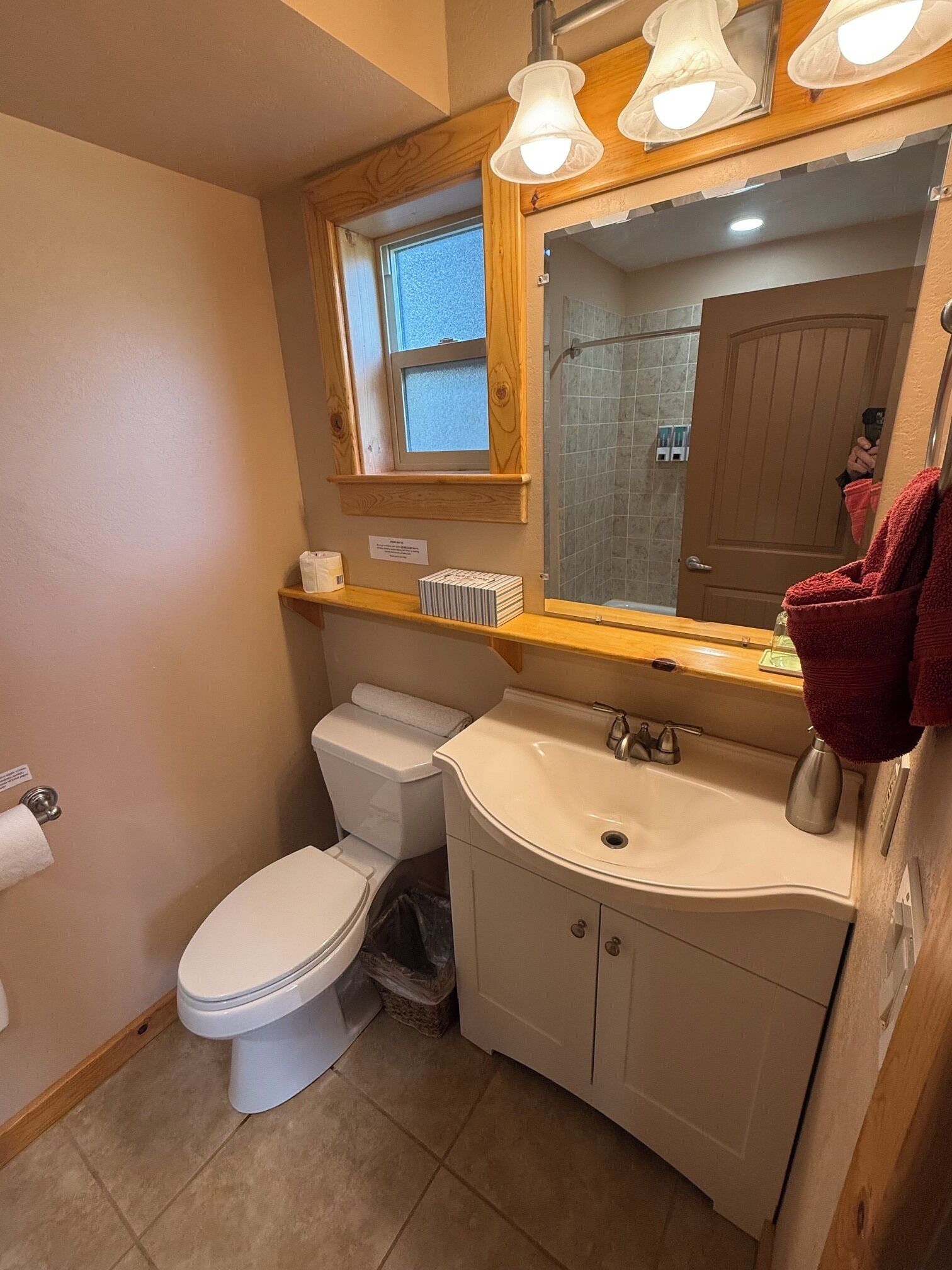 A bathroom with a toilet, sink, mirror, and window.