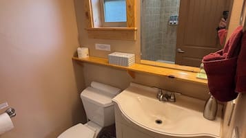 A bathroom with a toilet, sink, mirror, and window.
