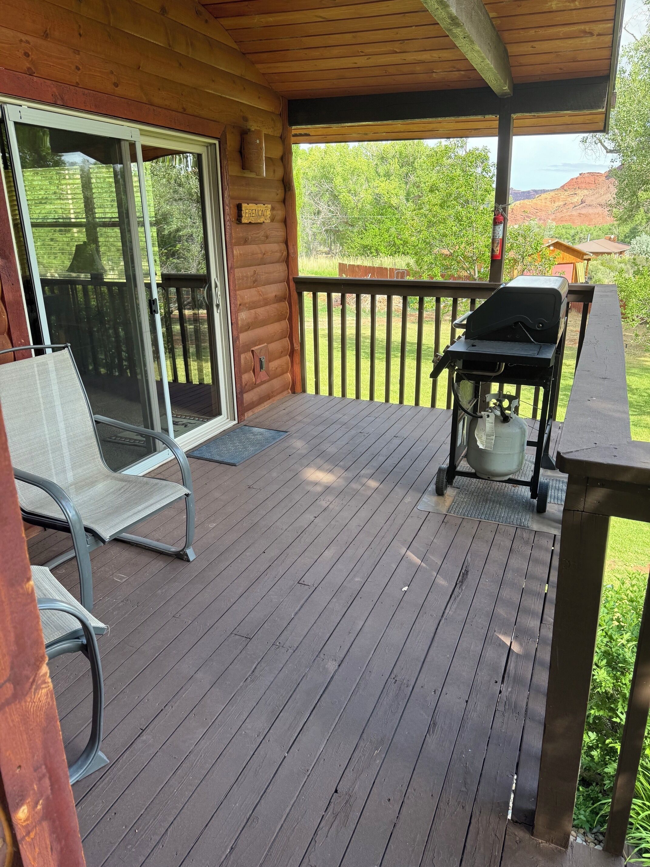 Una terraza de madera con una parrilla, una puerta corrediza de vidrio y una silla.
