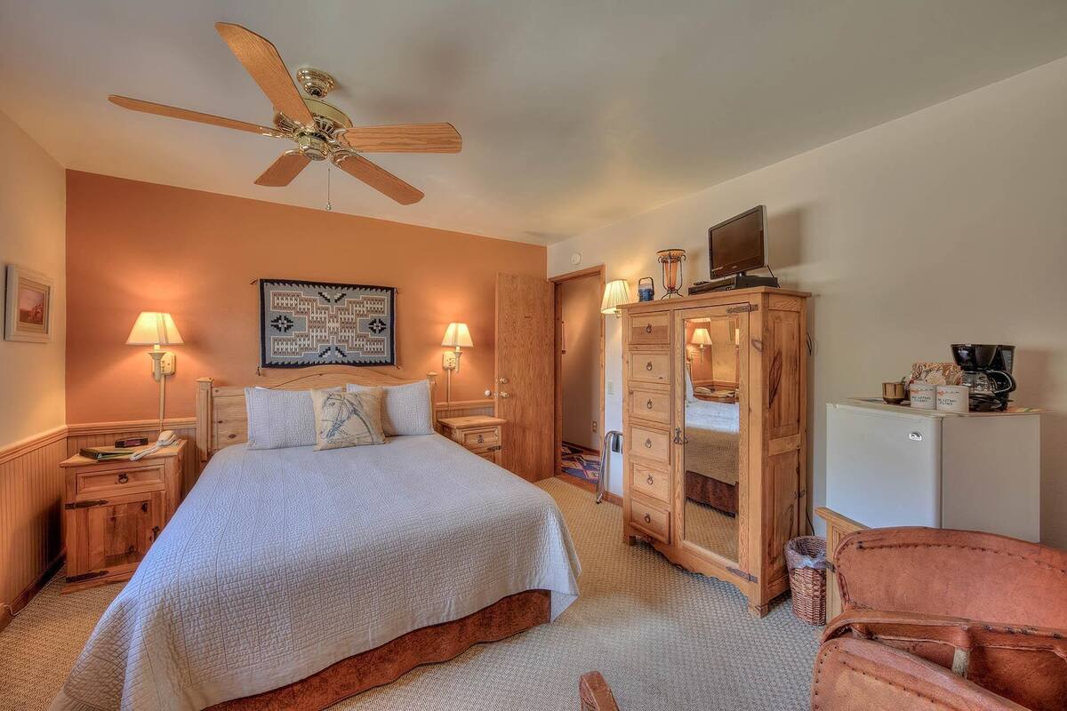 A bedroom with a bed, wooden wardrobe, ceiling fan, bedside lamps, and a television.