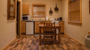 A compact kitchen with wooden cabinets, a microwave, a refrigerator, a stove, and a dining table with chairs.