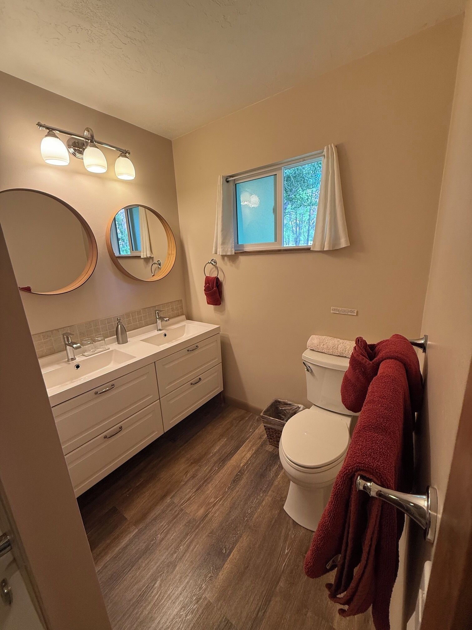 A bathroom with a vanity, a toilet, a window with curtains, and a mirror.