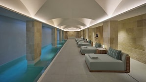 Un espace spa doté d’une longue piscine, de coins salon et de murs en pierre.