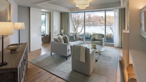 Un salon moderne comprenant un canapé, des fauteuils, une table basse et offrant une vue sur un lac grâce à de grandes fenêtres.