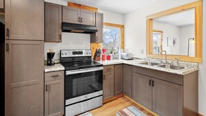 A modern kitchen with wooden cabinets, stainless steel appliances, a window, and a large mirror. - The Barn - Lake View and Pet Friendly (Pittsfield)