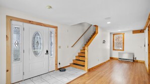 A spacious hallway with a wooden staircase, white tiled flooring, and a radiator. - The Barn - Lake View and Pet Friendly (Pittsfield)