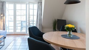 Un coin repas avec une table ronde, des chaises, un vase rempli de fleurs jaunes et un luminaire suspendu noir.
