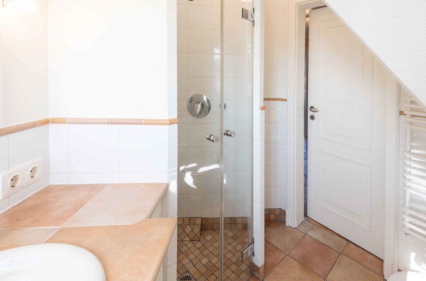 Ein Badezimmer mit Duschkabine aus Glas, Toilette und Waschbecken mit beiger Arbeitsplatte.
