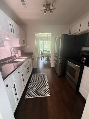 Eine Küche mit weißen Schränken, einer schwarzen Arbeitsplatte, einem gemusterten Teppich, einem Kühlschrank und einem Backofen.