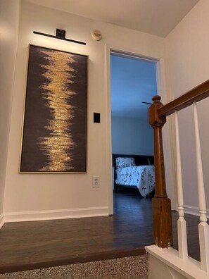 A staircase with a wooden handrail and white balusters, leading to a bedroom with a bed and a nightstand. - Highland Park Beauty Walkable to Rojo and Parks! (Birmingham)