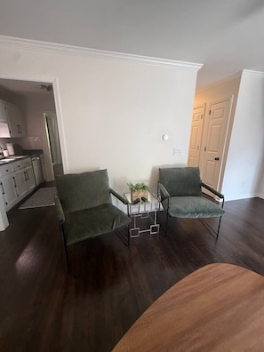 A room with two green upholstered chairs, a small side table with a plant, and a wooden table. - Highland Park Beauty Walkable to Rojo and Parks! (Birmingham)