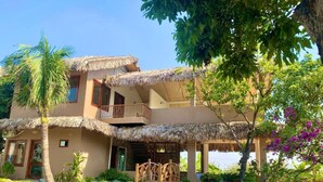 A two-story building with a thatched roof, a swimming pool, and lush greenery. - Lemon Tree Homestay Tam Coc (Nam Hoa Lu)