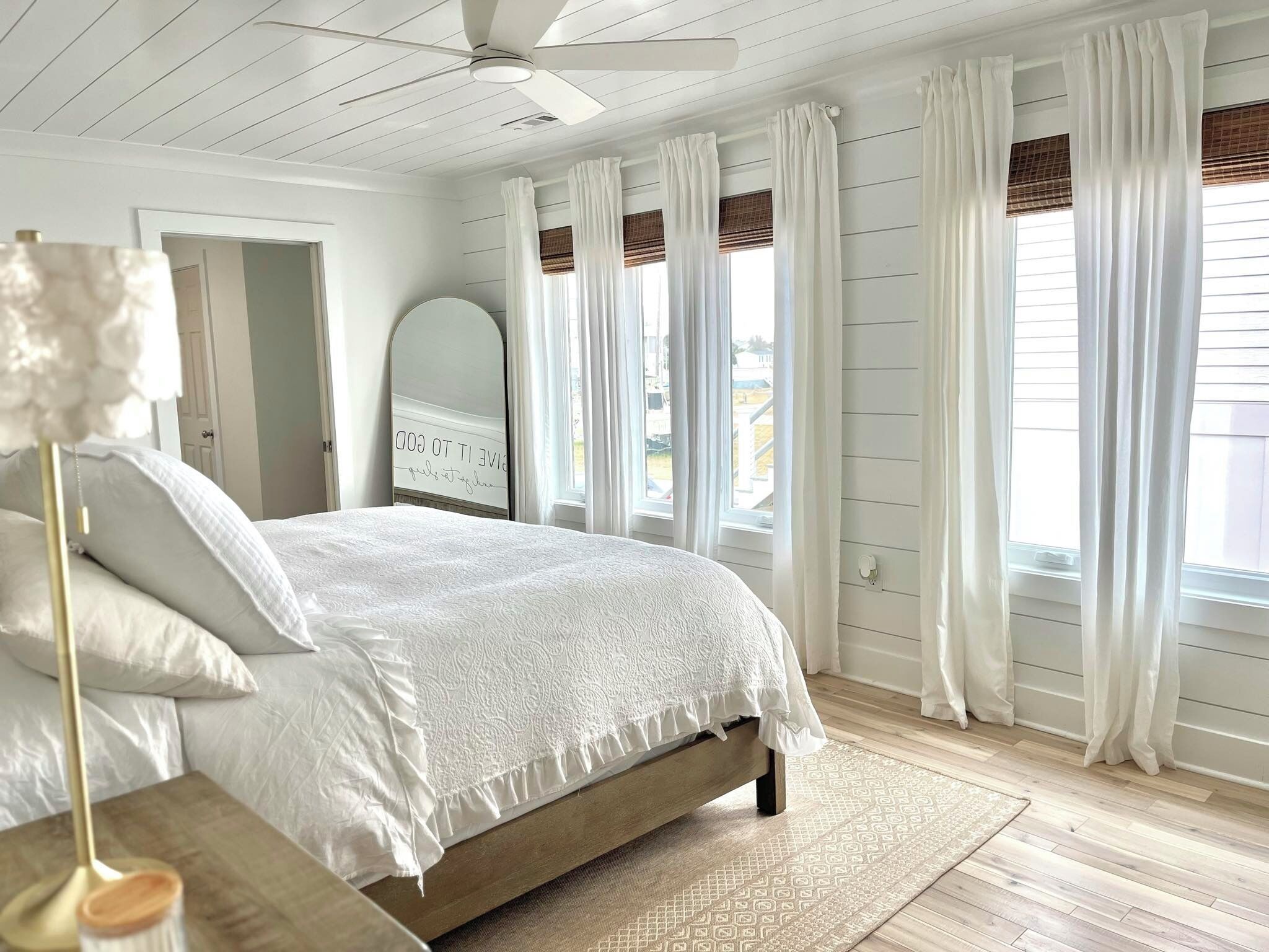 A bedroom with a bed, a ceiling fan, and a window with curtains.