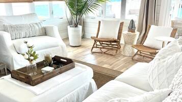 Amplia sala de estar con un sofá blanco, una mesa de centro de madera con objetos decorativos, una planta grande en maceta y un sillón de mimbre.
