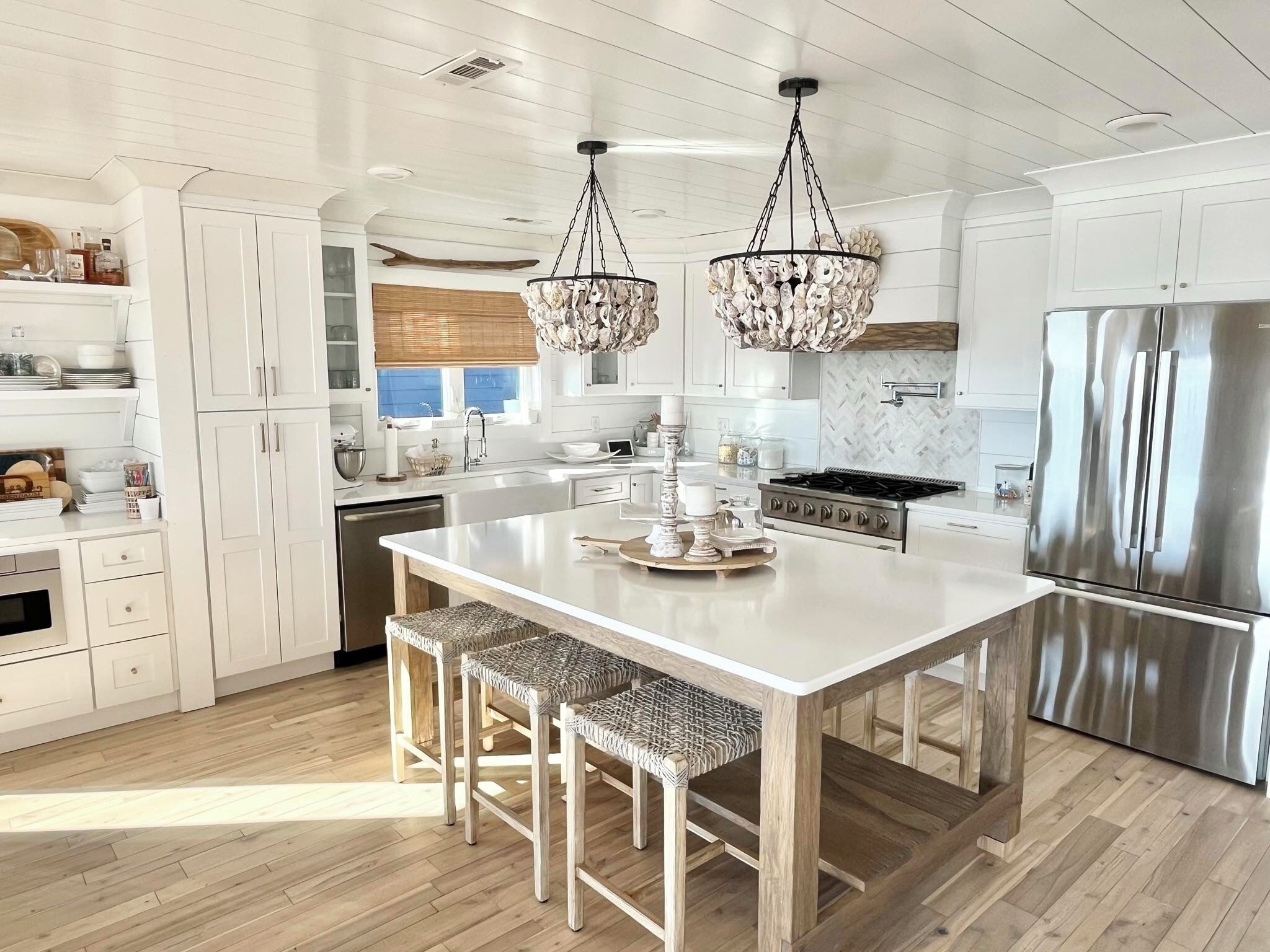 A modern kitchen with white cabinetry, a central island with bar stools, a stainless steel refrigerator, and a unique chandelier.