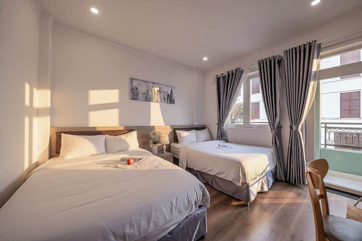 A hotel room with two beds, a nightstand, a chair, and a window with curtains.