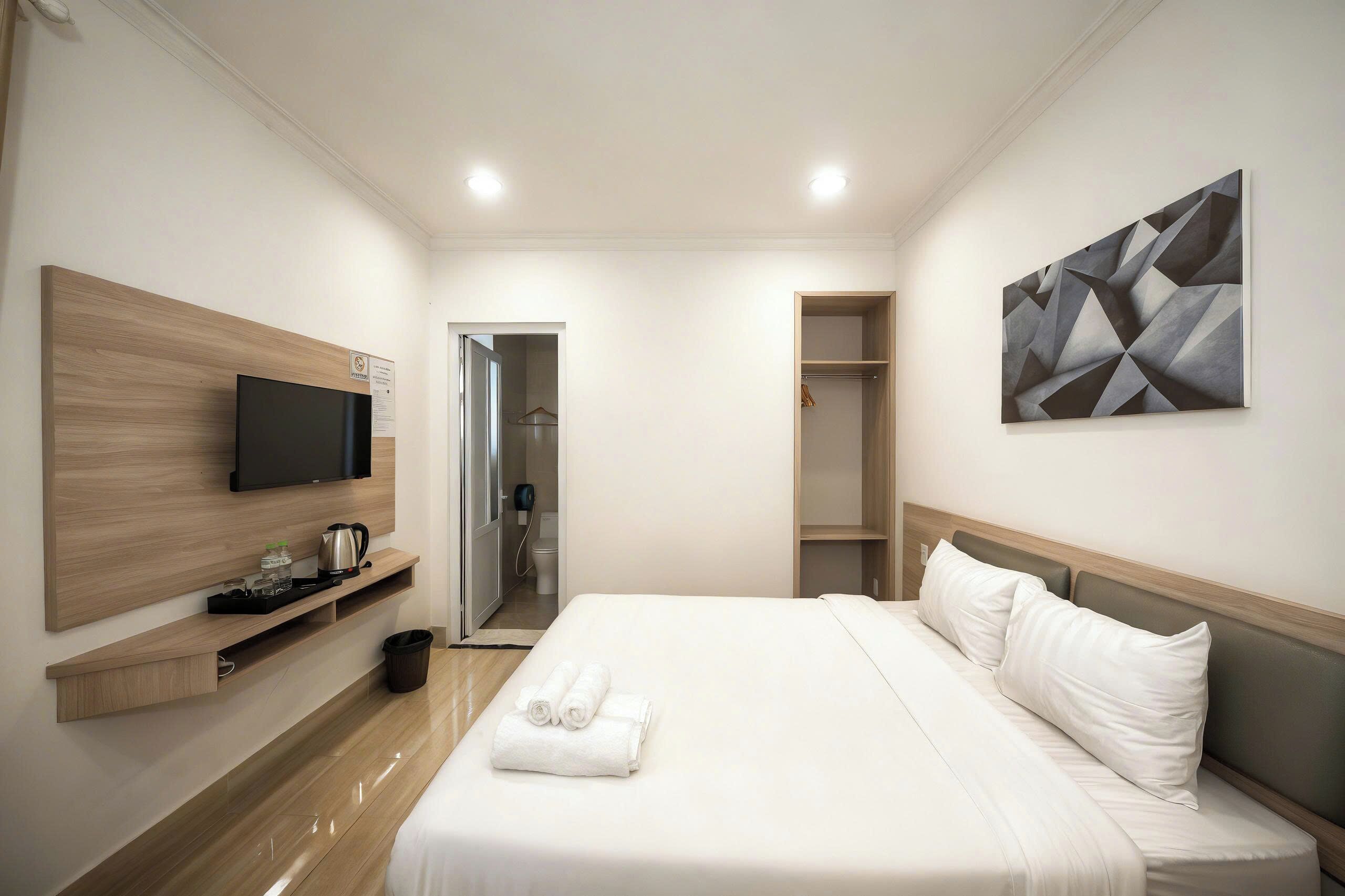 A hotel room with a bed, a TV, a coat rack, and a bathroom visible through an open door.