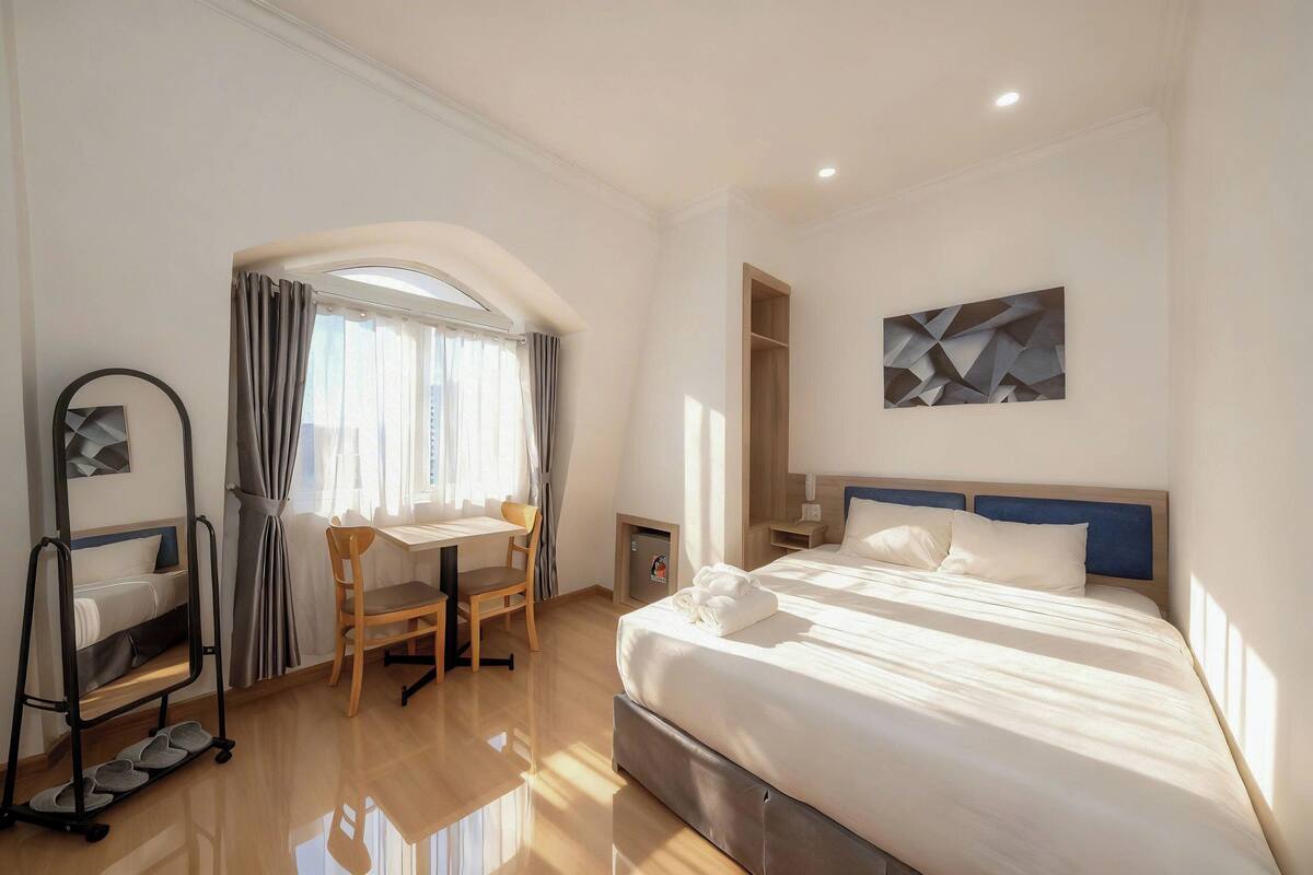 A hotel room with a bed, desk, chair, and a shoe rack.