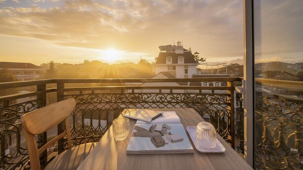 Un balcón con vista a una puesta de sol, una mesa con un cuaderno, un bolígrafo y un vaso.