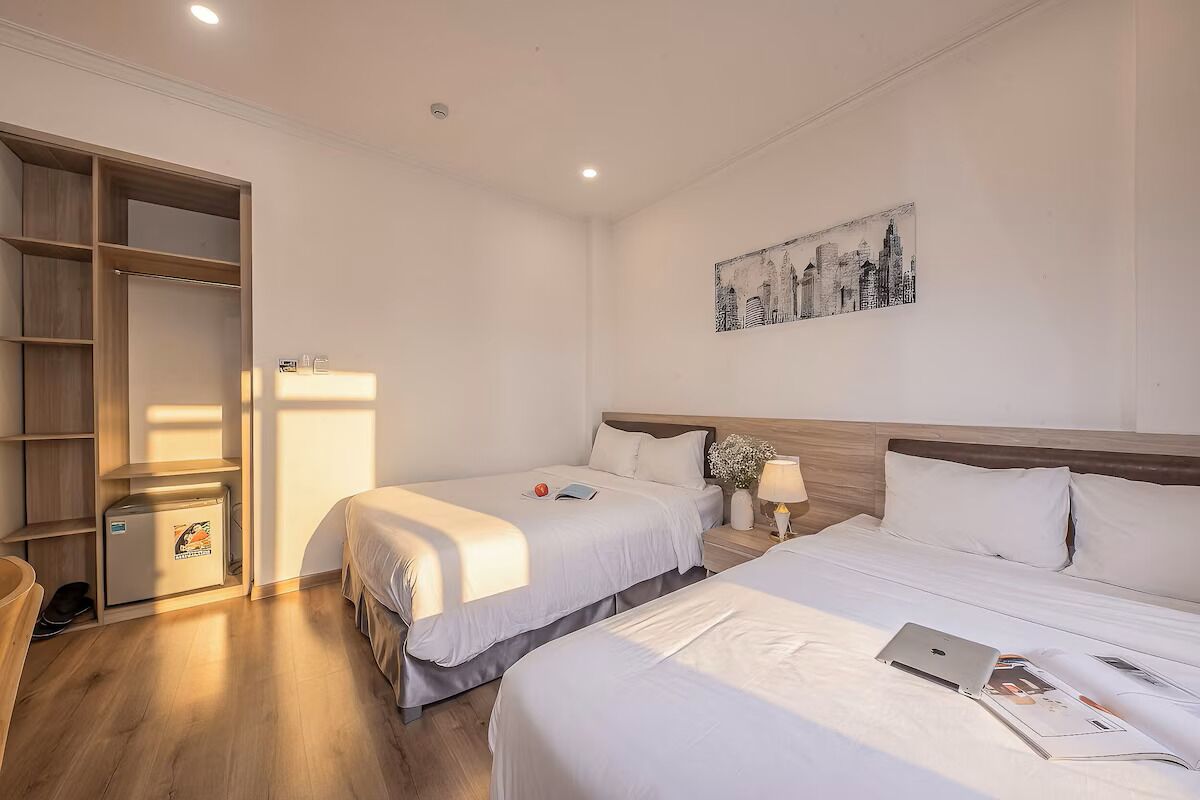 Habitación de hotel con dos camas, un armario, un escritorio con lámpara y una obra de arte con vista a la ciudad.