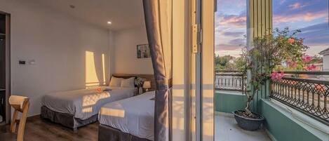 A bedroom with two beds, a wooden chair, a balcony with a railing, and a potted plant.