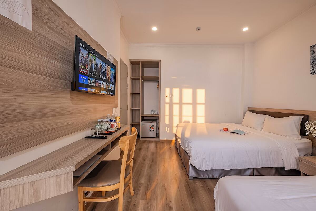Quarto de hotel com uma cama, uma escrivaninha com cadeira, televisão fixada na parede e um armário.