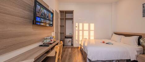 Quarto de hotel com uma cama, uma escrivaninha com cadeira, televisão fixada na parede e um armário.