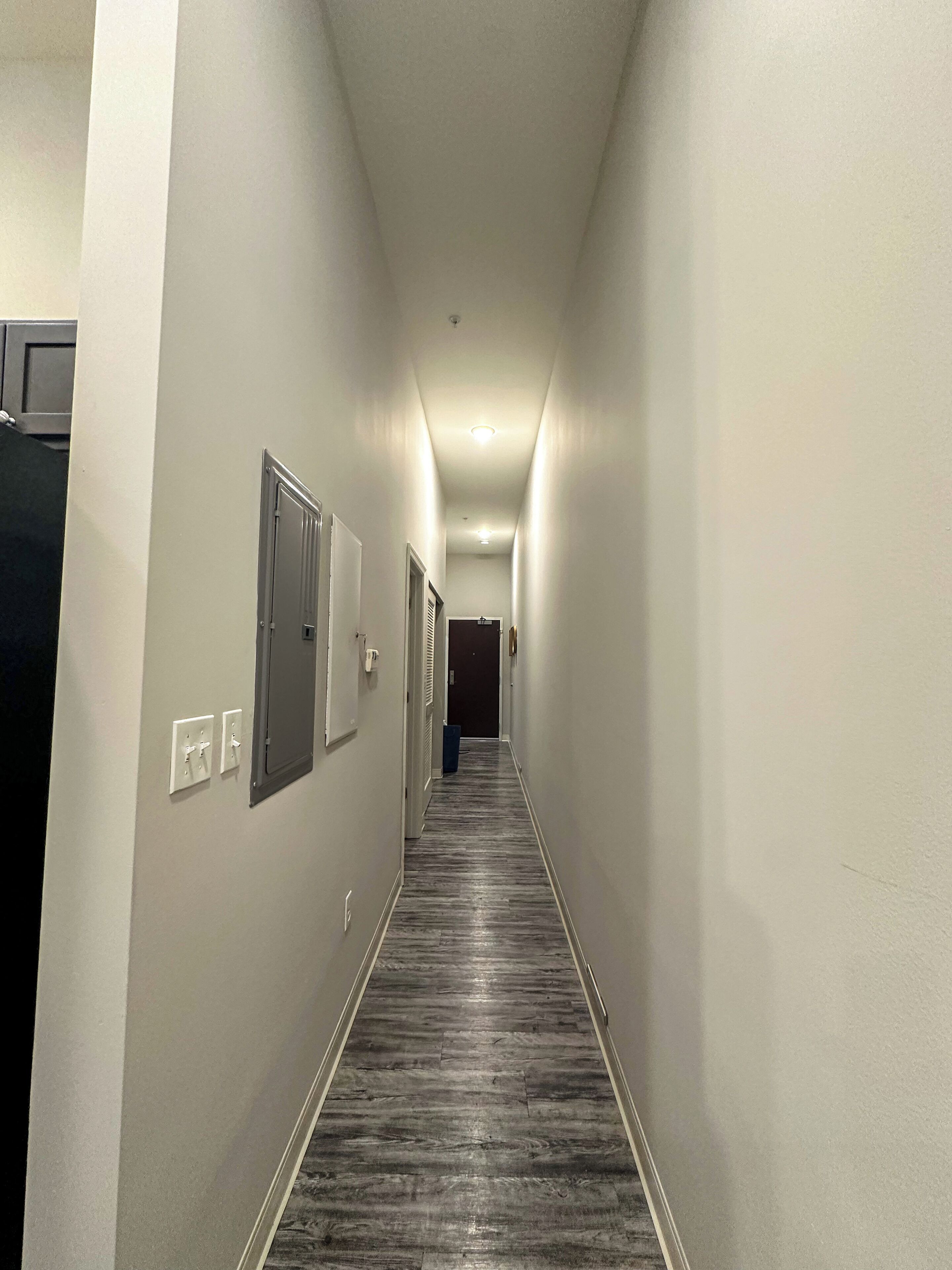A narrow, well-lit hallway with a wooden floor, white walls, and several doors along the sides.