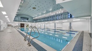 Une piscine intérieure avec un sol carrelé, un escalier d’accès et un plafond doté de luminaires circulaires.