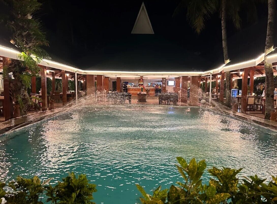 Een nachtzicht van een hotelzwembad met een overdekte zithoek en een bar.
