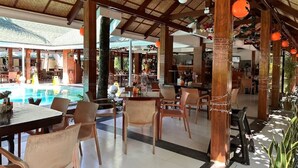 Ein überdachter Essbereich im Freien mit Tischen und Stühlen, ein Pool und eine Bar.