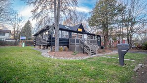 A log cabin with a wooden deck and a staircase leading to the entrance. - Timber Lodge: Hot Tub, Fireplace & Fun for All ! (West Milford)