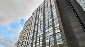 A modern high-rise building with a glass facade and a parking area in front. - Despierta con vista a la montaña (Bogotá)