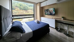 A modern bedroom with a large bed, a TV mounted on the wall, and a view of the outdoors. - Despierta con vista a la montaña (Bogotá)