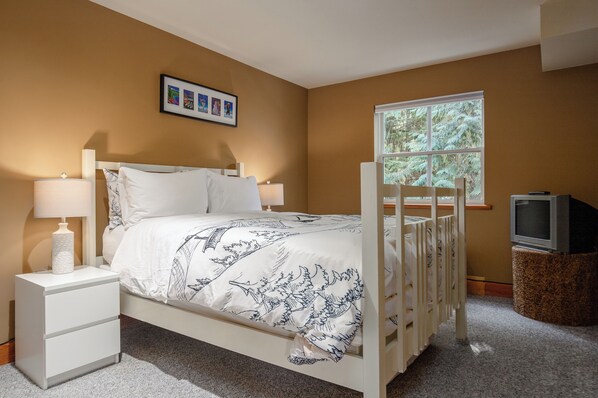 A bedroom with a bed, nightstands, a TV, and a window with a view of trees. - Well furnished 3-bedroom townhome in perfect location for ski or golf (Whistler)