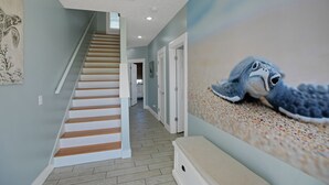 A hallway with a wooden staircase, a textured wall mural, and a bench. - Steps2Beach~Heated Pool~MiniGolf~Hot Tub~Game Room (Panama city)