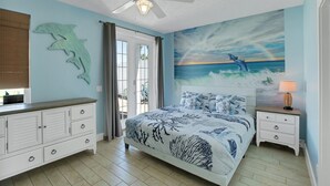 A bedroom with a bed, a nightstand, a dresser, a ceiling fan, and a mural of a dolphin and ocean scene. - Steps2Beach~Heated Pool~MiniGolf~Hot Tub~Game Room (Panama city)