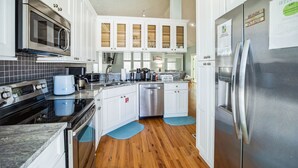 A modern kitchen with white cabinets, stainless steel appliances, and wooden flooring. - Steps2Beach~Heated Pool~MiniGolf~Hot Tub~Game Room (Panama city)