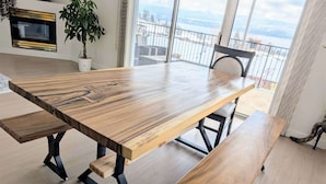 Un vaste espace dédié à la salle à manger, avec une grande table en bois et des bancs, une plante en pot, et une vue sur un paysage enneigé grâce à de grandes fenêtres.